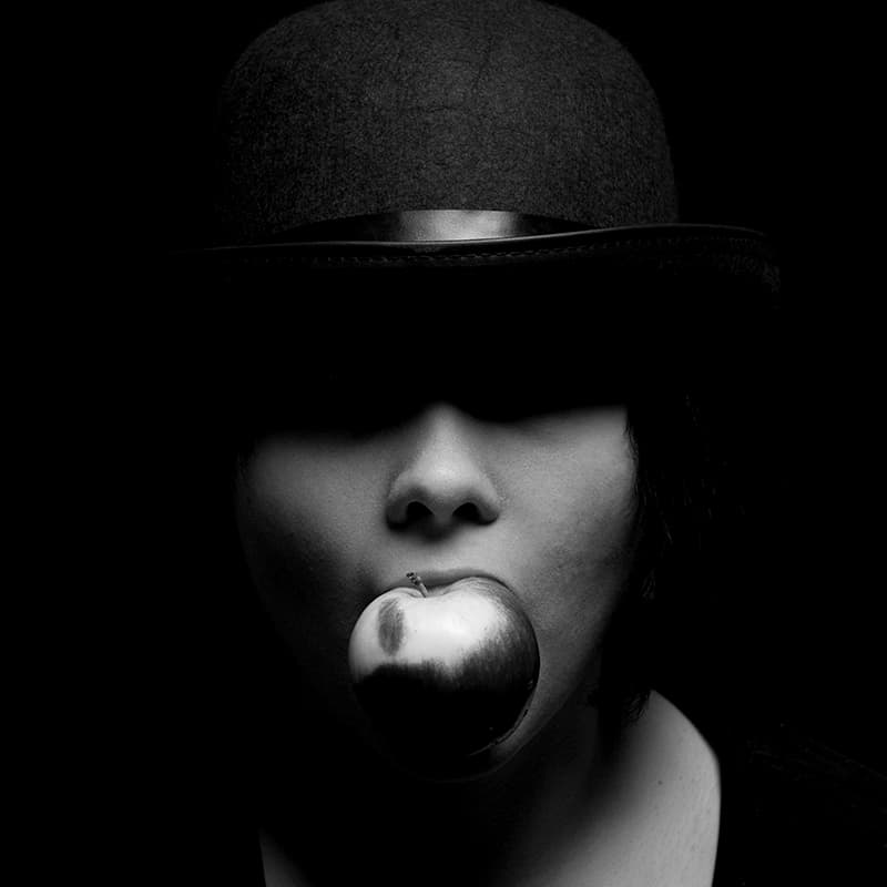 Black and white image of womn in hat with apple in mouth