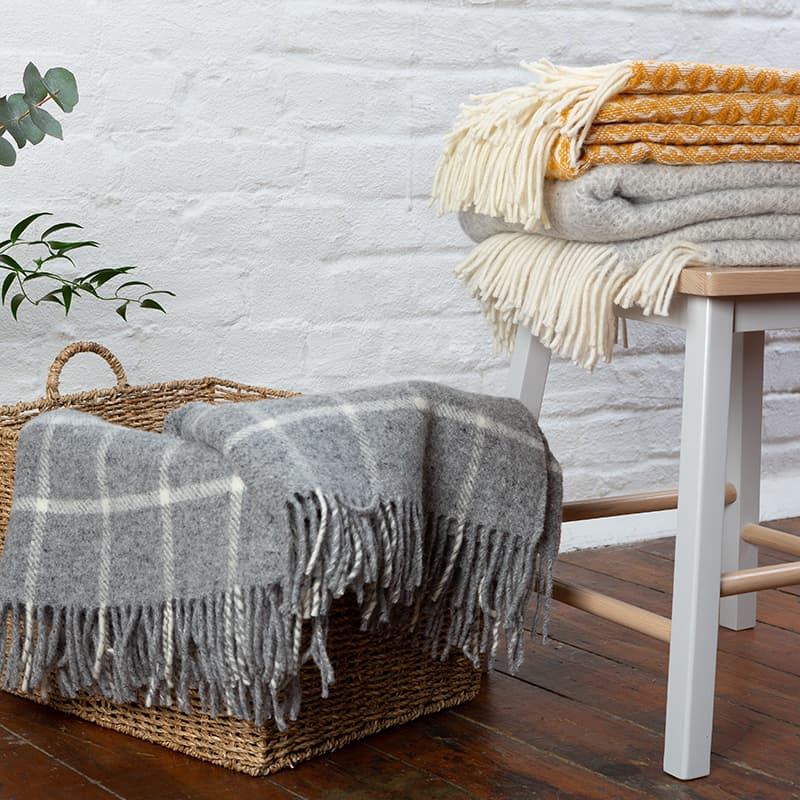 Three dark woolen blankets folded against a dark grey wall.