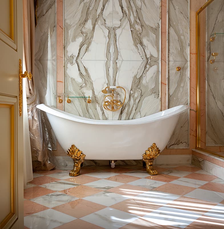 White free standing bath with gold feet on pink and grey marble floor.