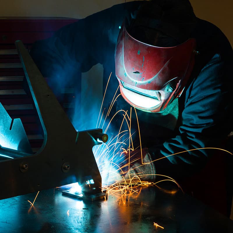 Close up of Welder welding wearing dark blue uniform with a dark red welding helmet.