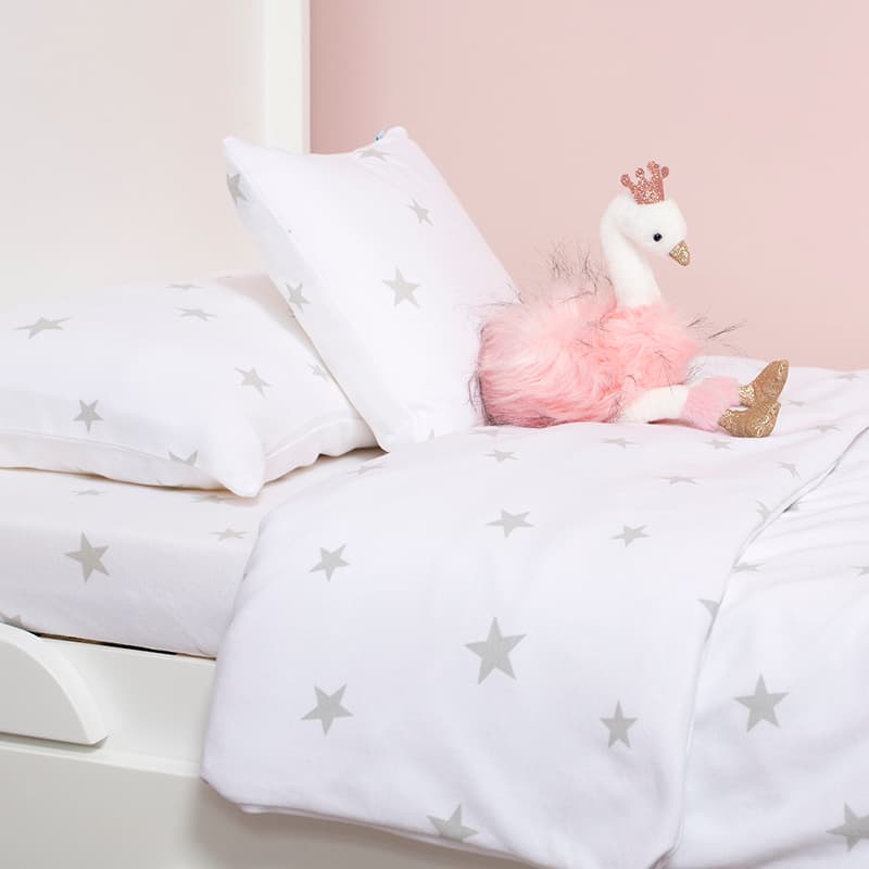 White bedding with silver stars with a pink and white swan soft toy sitting against one of the pillows.