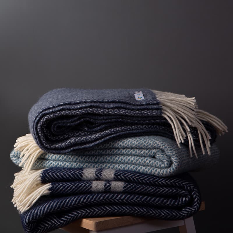 Three dark blue woolen blackets folded square in a pile on a stool