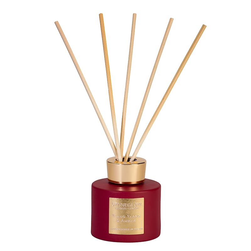 Drak red glass room diffuser with a gold top and natural reeds.