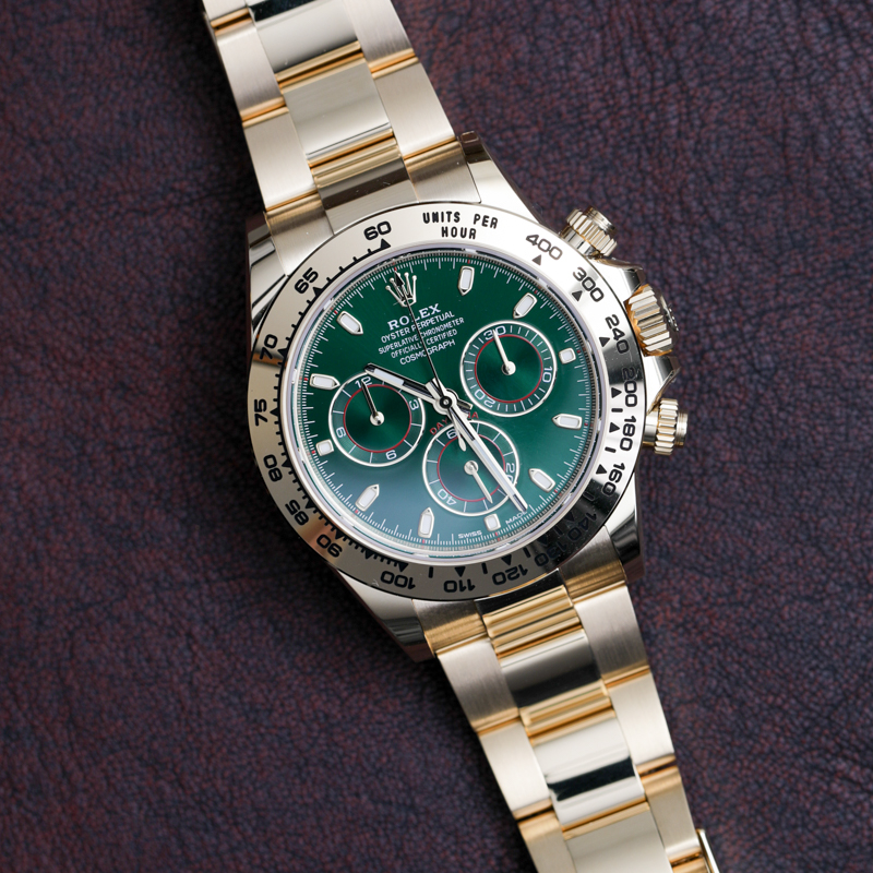 Gold Rolex watch laying flat with a green face